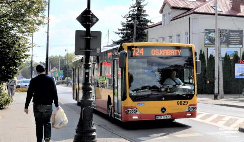 Ulica, po której jedzie czerwono-pomarańczowy autobus komunikacji miejskiej. Nad jego przednią szybą wyświetla się napis: 724 Metro Kabaty.