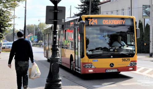 Ulica, po której jedzie czerwono-pomarańczowy autobus komunikacji miejskiej. Nad jego przednią szybą wyświetla się napis: 724 Metro Kabaty.