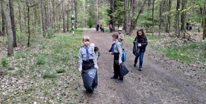 Grupa osób, harcerzy, z czarnymi workami na leśnej ścieżce zbiera śmieci.