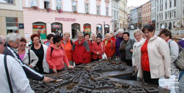 Na rynku starego miasta stoją starsze kobiety zgromadzone wokół metalowej makiety miasta