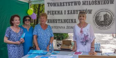 Cztery kobiety stojace pod namiotem na tle baneru Towarzystwa Miłośników Piękna i Zabytków Konstancina.