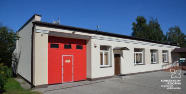 Długi parterowy budynek, po lewej stronie duże drzwi wjazdowe w kolorzez czerwonym