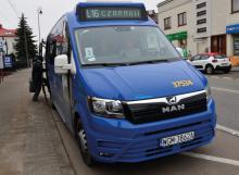 Niebieski bus stoi na przystanku, ma otwarte boczne drzwi, nad przednią szybą wyświetlacz z numerem linii L16 i nazwami przystanków – początkowego i końcowego – Czarnów.