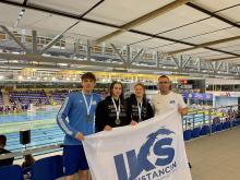 Cztery osoby stoją na tle basenu i w rękach trzymają baner z logo IKS Konstancin