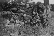 Czarno-białe zdjęcie. Na nim dziesięciu młodych męzczyzn w polskich mundurach z okresu II wojny światowej. W rękach trzymają karabiny, pozują do zdjęcia. Po prawej ich stronie leży na trawie młoda dziwewczyna, uśmiecha sie i tez pozuje do zdjęcia.