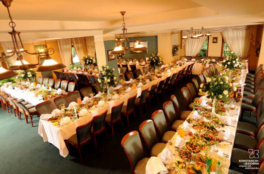 Wnętrze duzej sali restauracyjnej ze stolikami ustawionymi na potrzeby przyjęcia weselnego, białe obrusy, nakrycia na stołąch, dekoracje