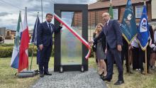 Uroczyste odsłonięcie pomnika upamiętniającego, z udziałem oficjeli i pocztów sztandarowych, odbywa się przy asyście flag narodowych i lokalnych.