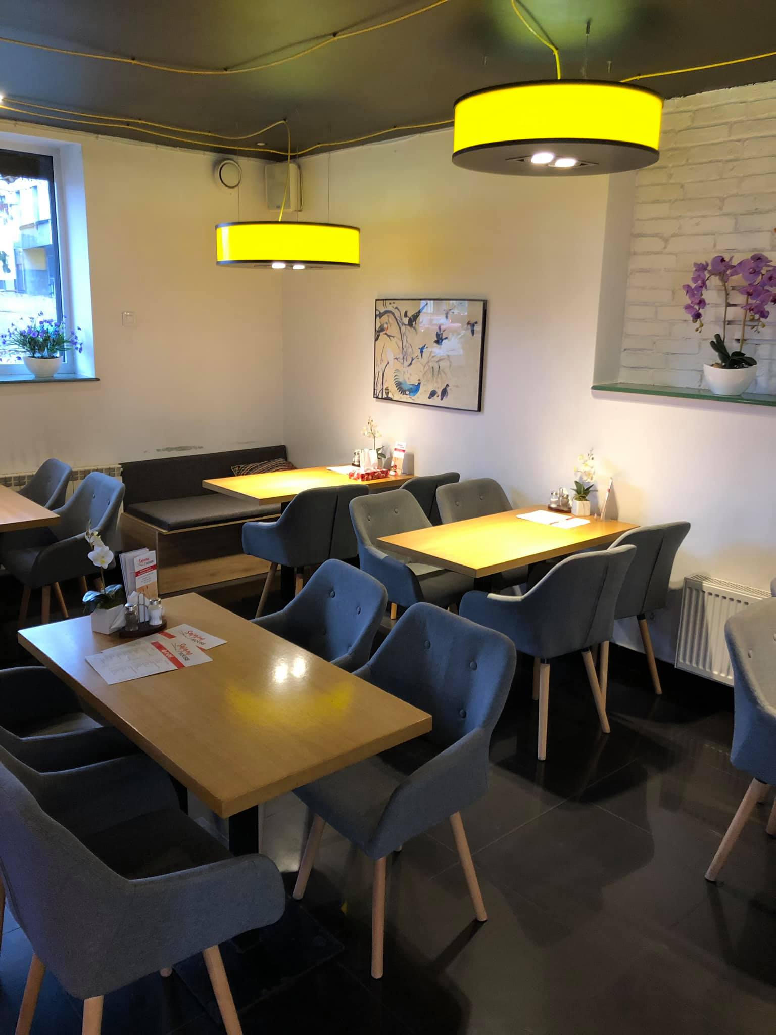 Wnetrze lokalu gastronomicznego, stoliki i foteliki, na ścianach dekoracje, spod sufitu zwisają duże lampy