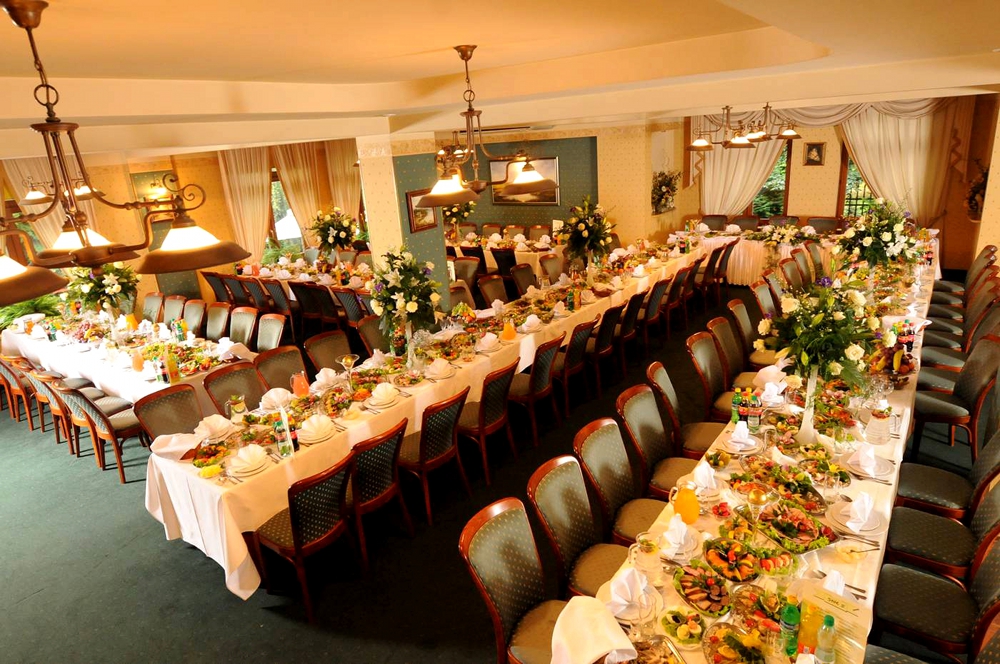 Wnętrze duzej sali restauracyjnej ze stolikami ustawionymi na potrzeby przyjęcia weselnego, białe obrusy, nakrycia na stołąch, dekoracje