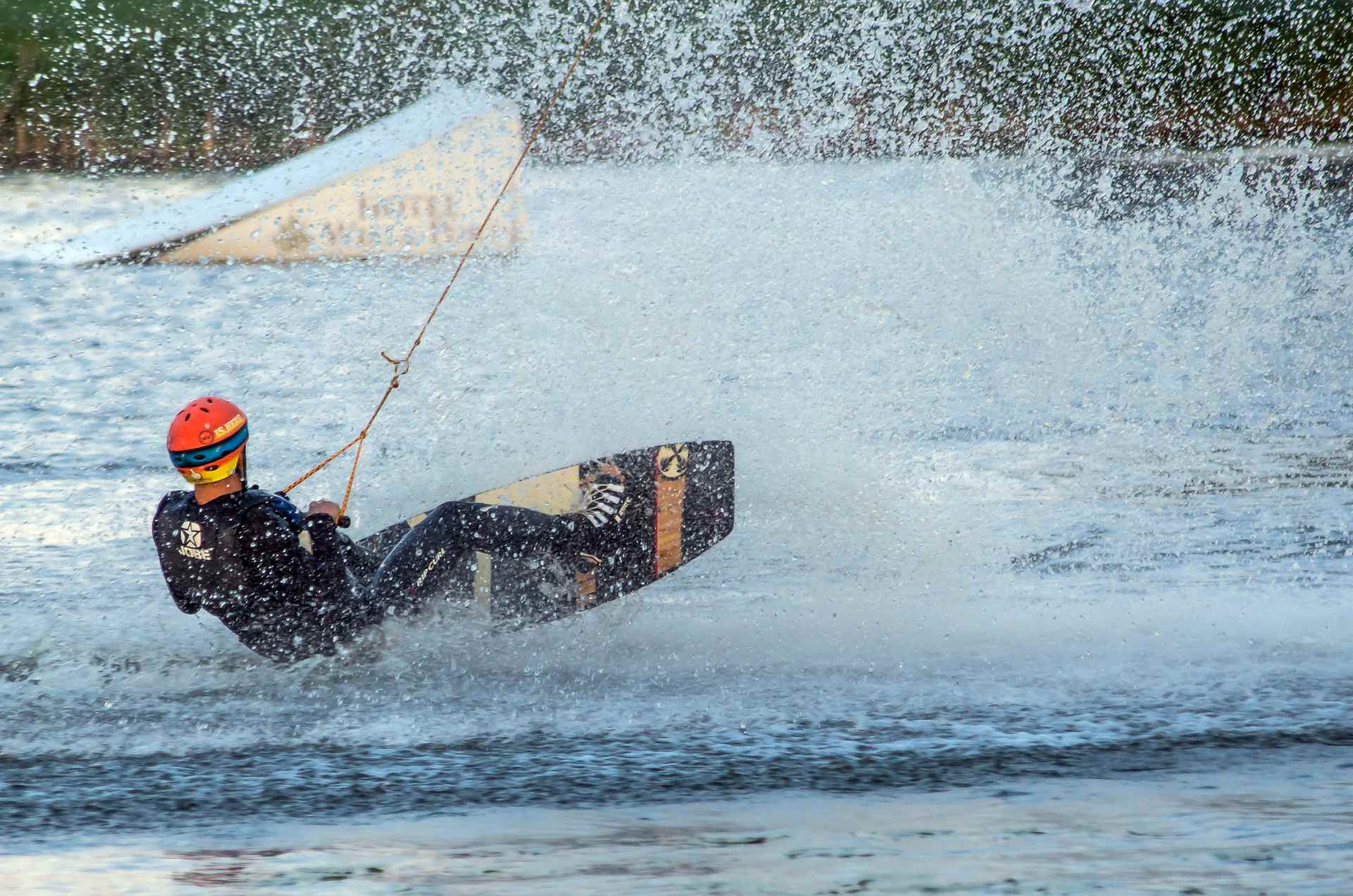Mężczyzna na desce do wakeboardingu ciągnięty przez wyciąg, rozpryskująca się woda. 