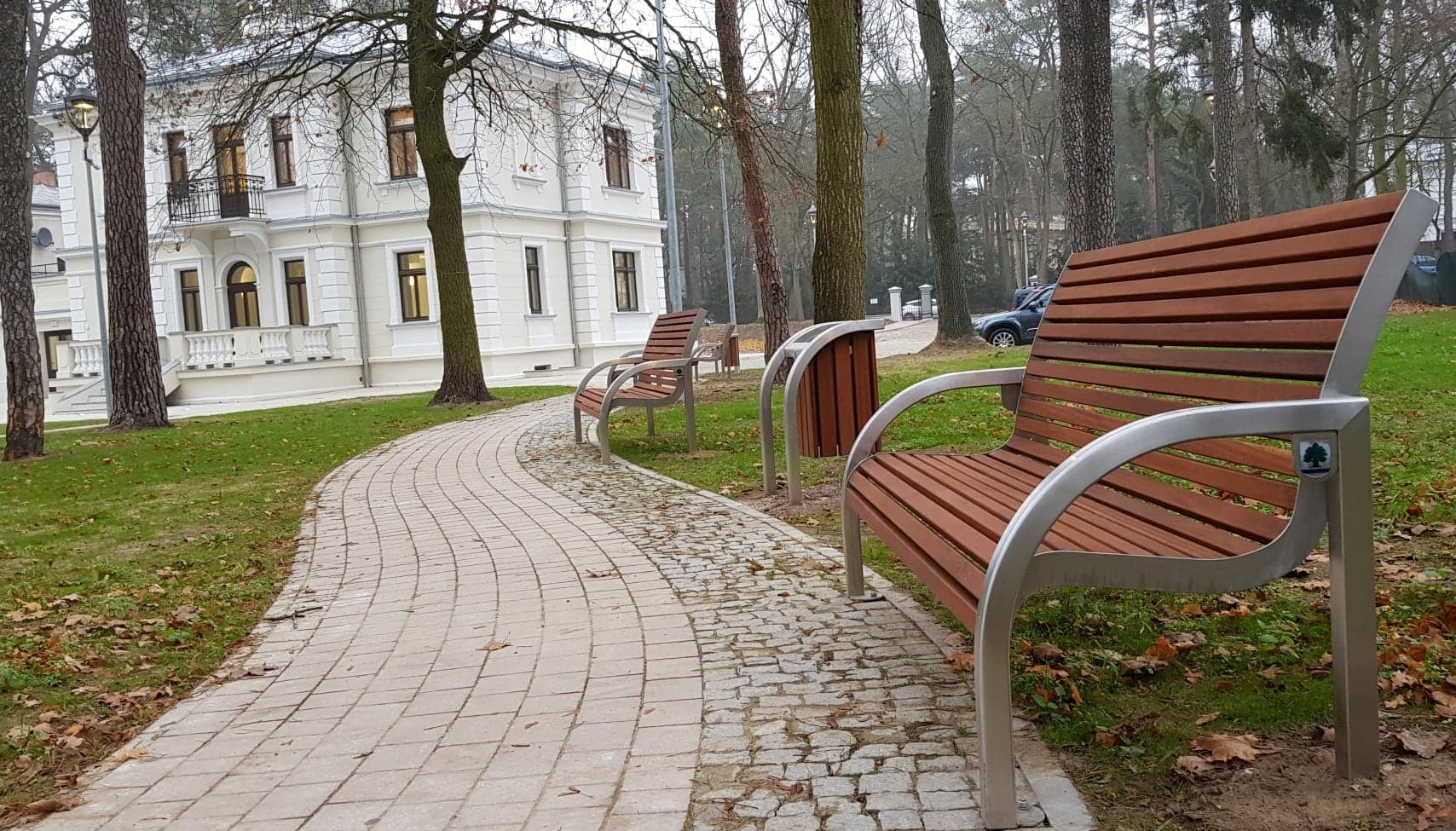 Ścieżka spacerowa prowadząca do willi Kamilin, którą widać w głębi zdjęcia. Po prawej stronie, przy  ścieżce stoją ławki parkowe. 