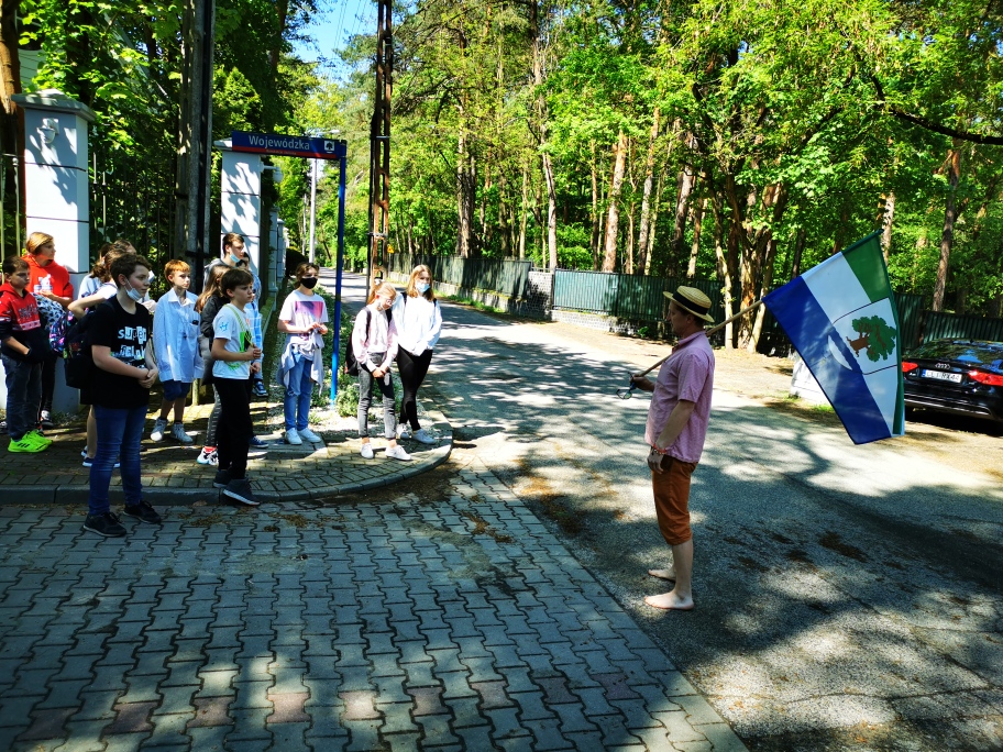 Grupa uczniów stojąca wraz z przewodnikiem podczas pieszej wycieczki.