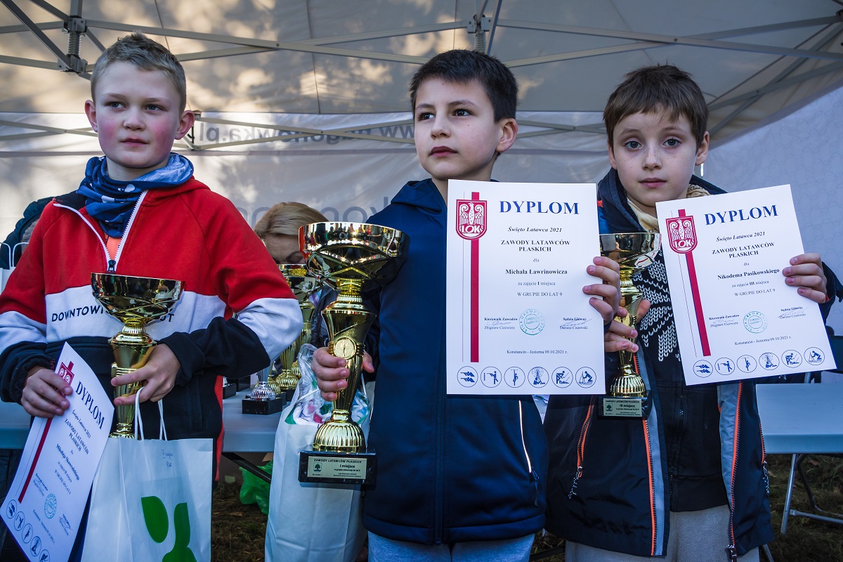 Trzech chłopców w wieku szkolnym stoi obok siebie w rzędzie. W rękach trzymają dyplomy i złote puchary.