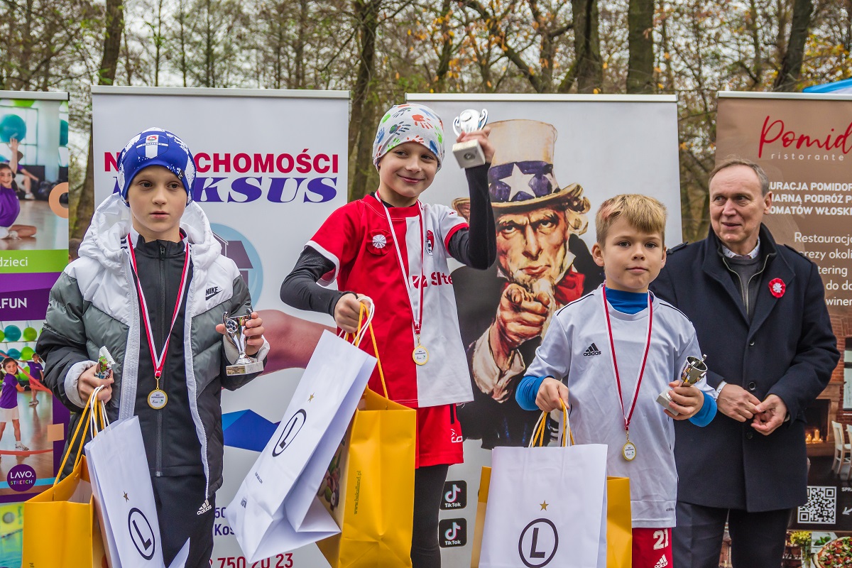 9.	Trzech chłopców w strojach sportowych,  z pucharami  w rękach i medalami na szyi. Za nimi stoi mężczyzna.