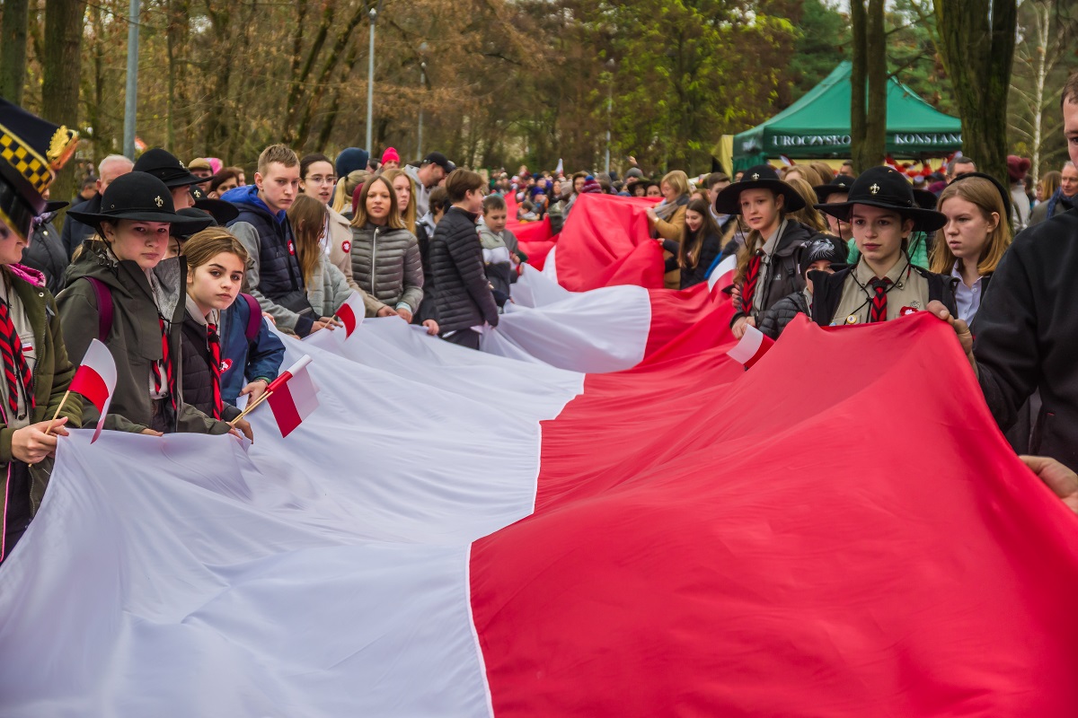 Tłum młodzieży i dzieci w parku, którzy trzymają 100-metrową biało-czerwona flagę.