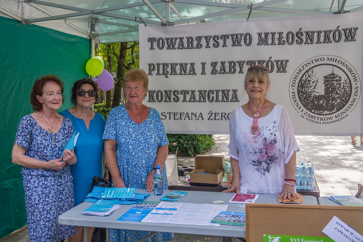 Cztery kobiety stojace pod namiotem na tle baneru Towarzystwa Miłośników Piękna i Zabytków Konstancina.