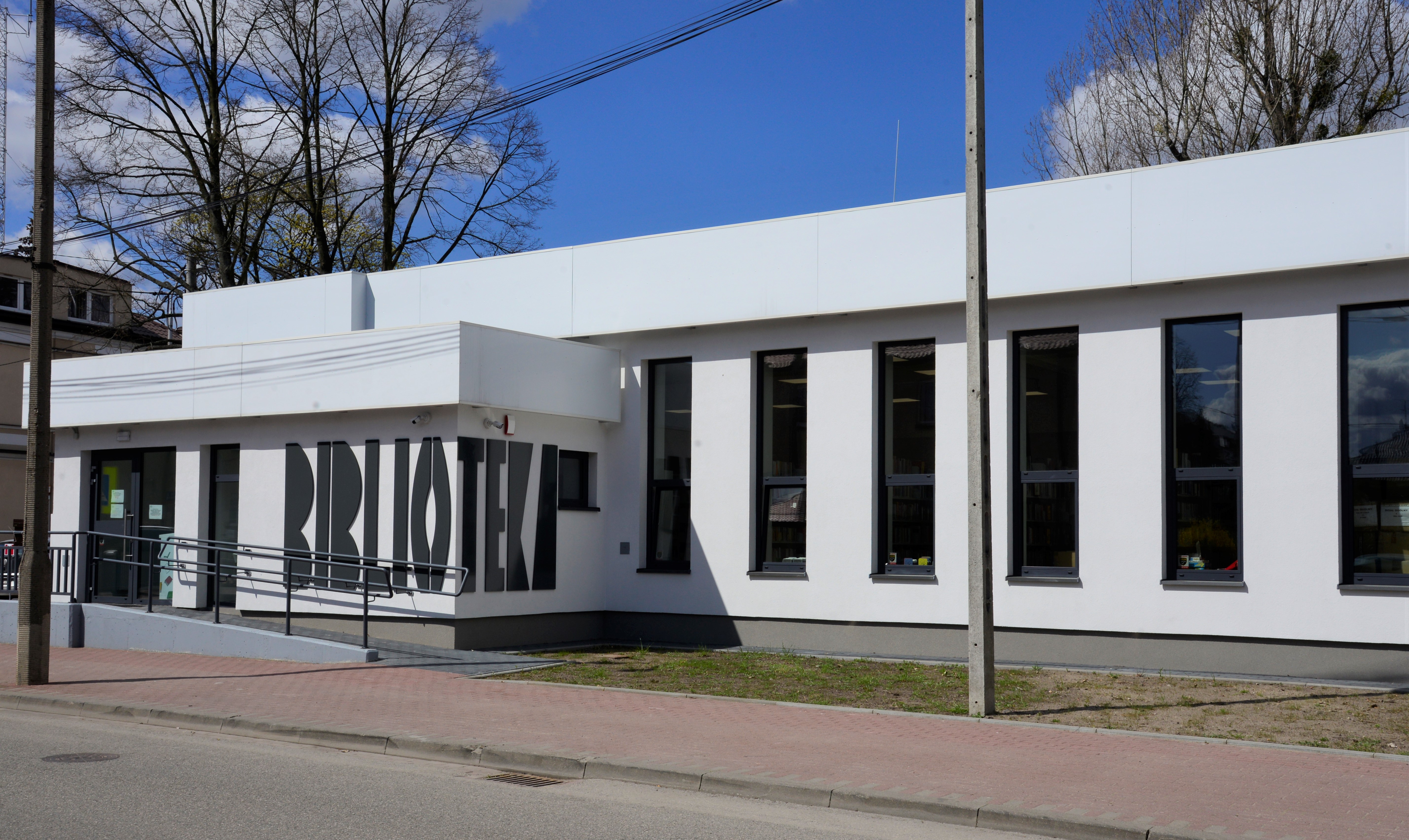 Niski, długi budynek z pionowymi dużymi oknami i gankiem z napisem BIBLIOTEKA