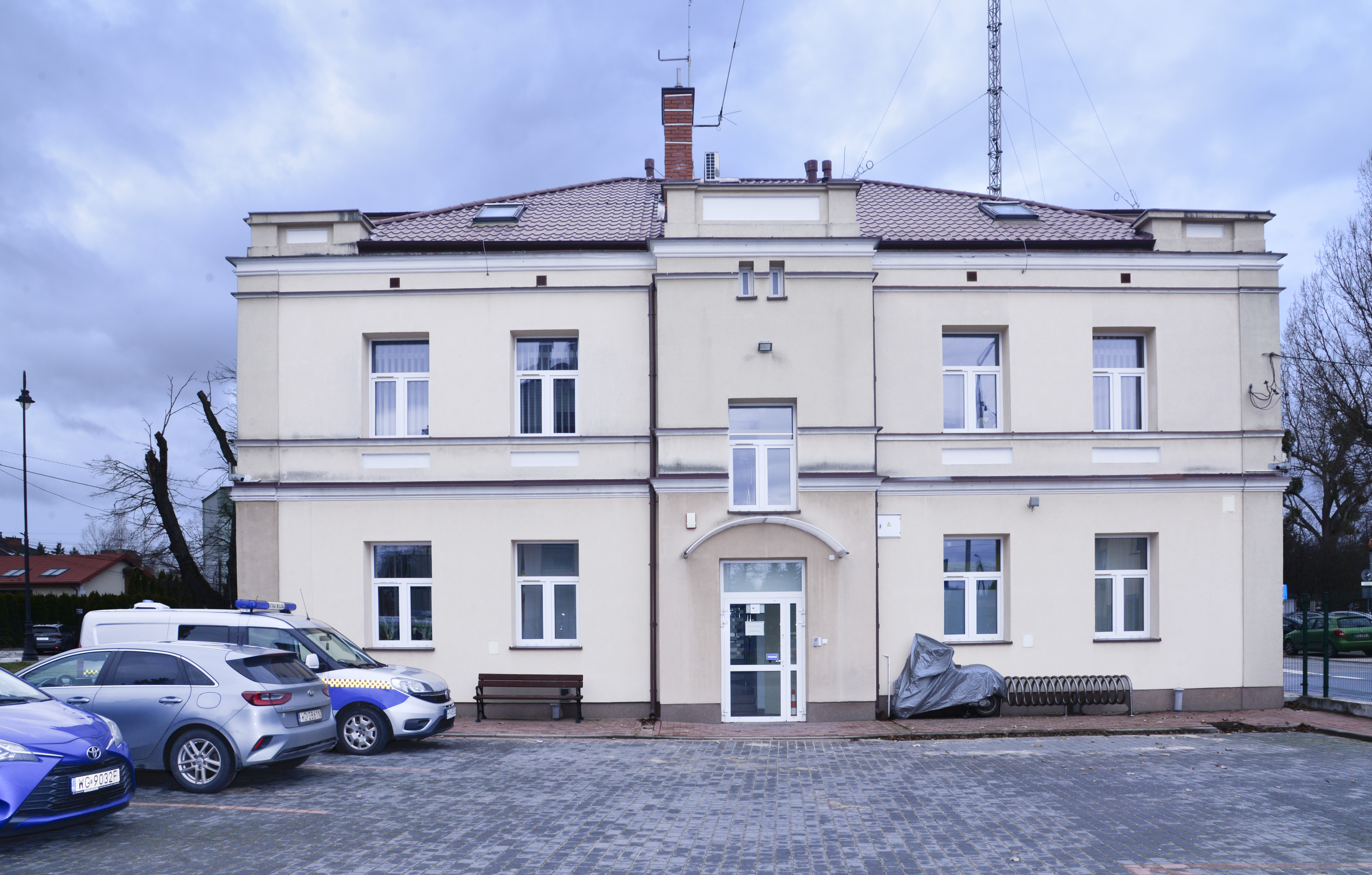 Piętrowy budynek widoczny od strony dużego placu, ściany jasne, dach spadzisty w kolorzez ciemnoczerwonym
