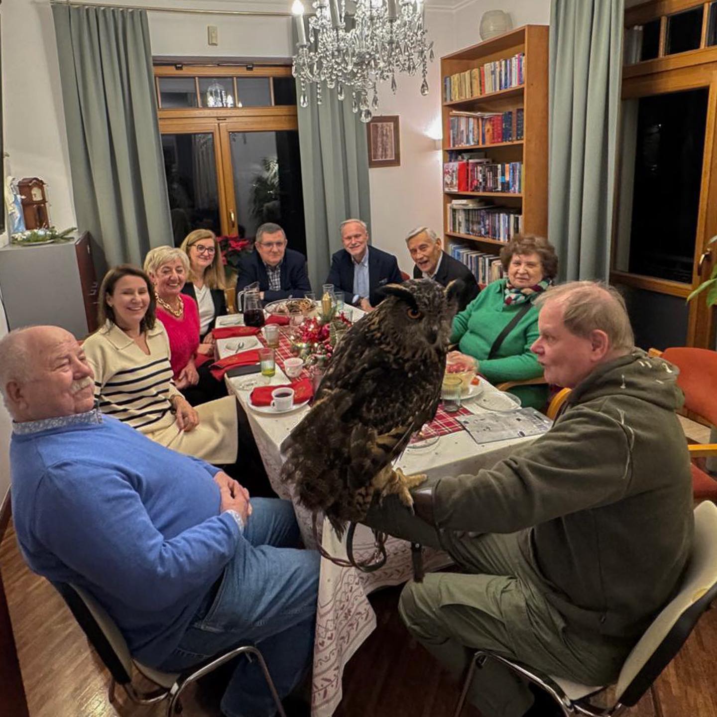 Uczestnicy świątecznego spotkania stoją wokół stołu w sali urzędu, słuchając opowieści o sowach, które znajdują się na środku pomieszczenia.