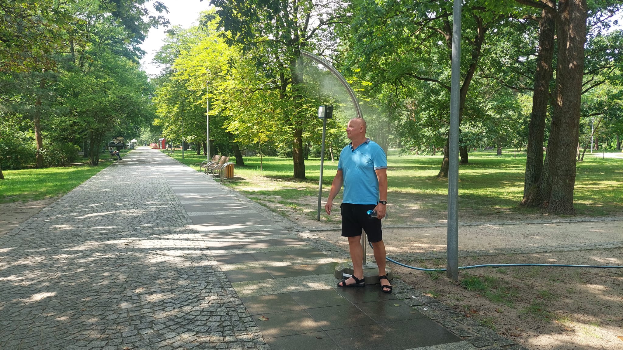Mężczyzna ochładza się pod słupkiem zraszającym podczas spaceru po Parku Zdrojowym.