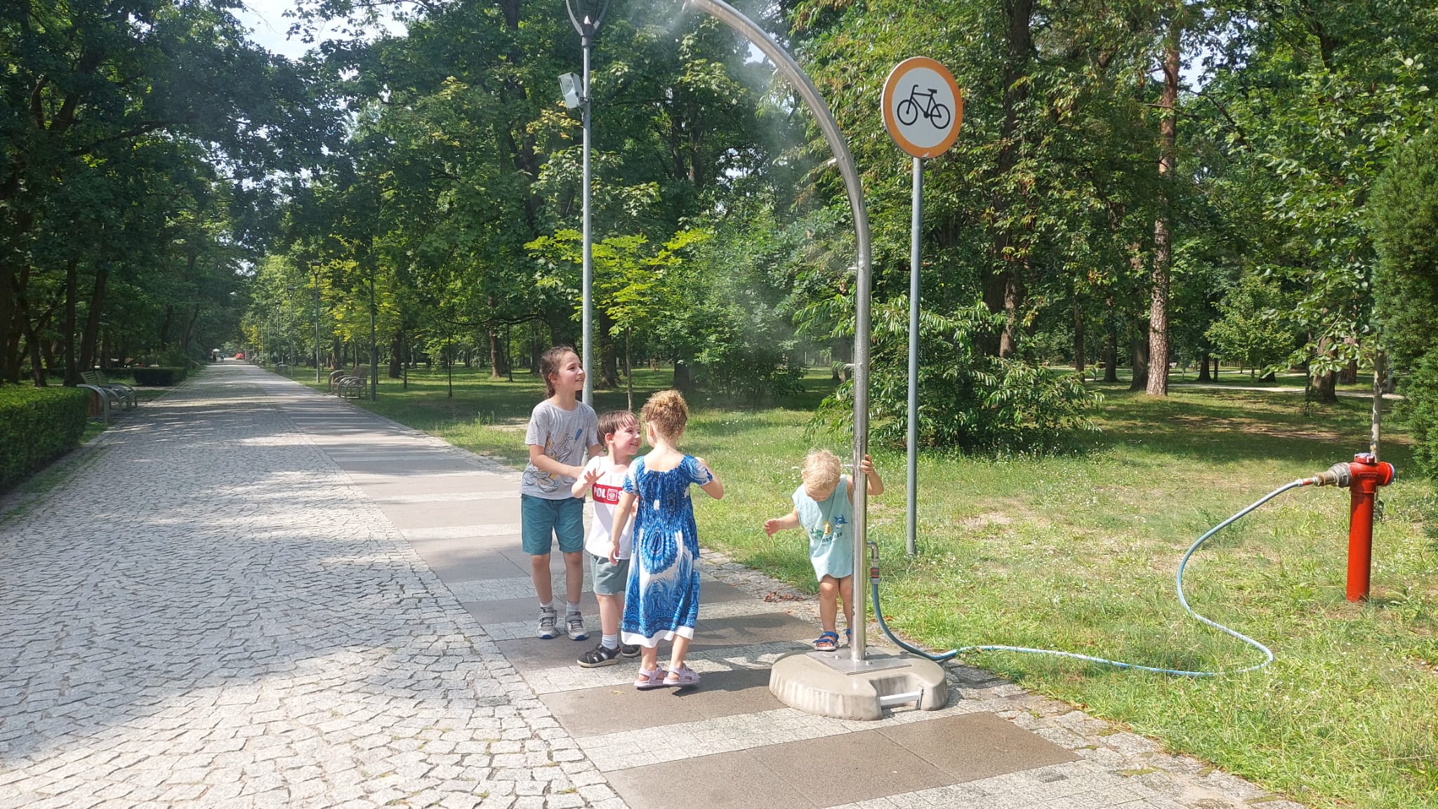 Dzieci bawią się i ochładzają pod słupkiem zraszającym w Parku Zdrojowym.