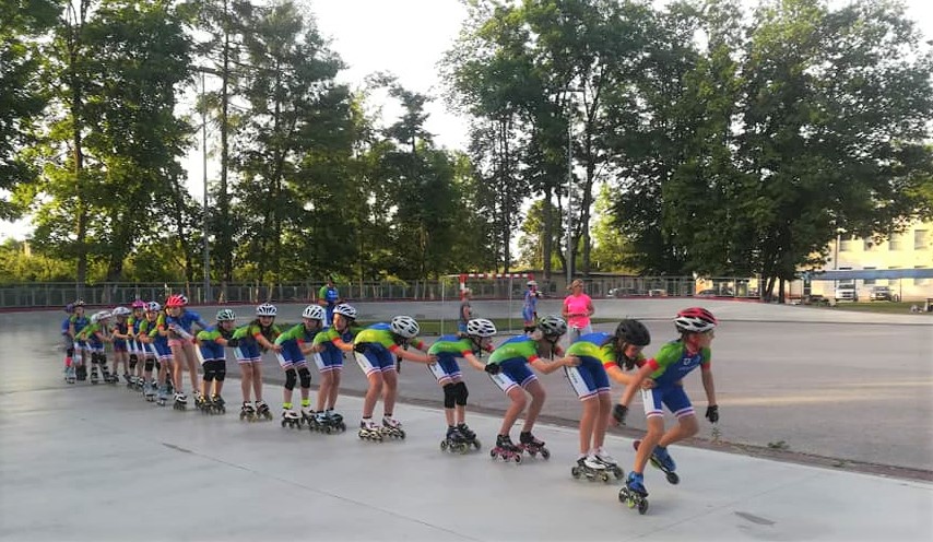 Zdjęcie przedstawia około 20 wrotkarzy z Uczniowskiego Klubu Sportowego Zryw Słomczyn. Ubrani są na sportowo, mają kaski i rolki. Jadą w grupie po betonowym torze