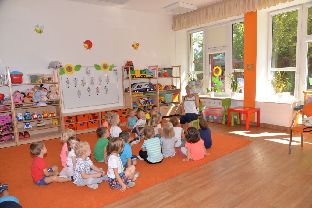 Grupa dzisci dziedząca na podłodze słuchająca wychowawcę na sali zabaw przedszkola