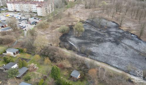 Widok z lotu ptaka, z lewej widoczne bloki mieszkalne, po prawej duży obszar wypalonej trawy, na dole widoczne małe domki na ogródkach działkowych