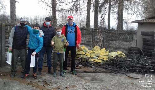 Trzech dorosłych mężczyzn i dwójka chłopc, wszyscy stoją, wszyscy w maseczkach na twarzy, obok po prawej wypełnione plastikowe worki i inne odpady