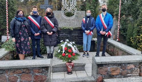 pięć osób stojących obok kamiennego pomnika. Na pomniku ułożona biało-czerwona wiązanka kwiatów.