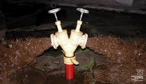 Stojak z dwiema głowicami podłączony do hydrantu wystającego z gruntu, z głowic wylewają się nieczystości
