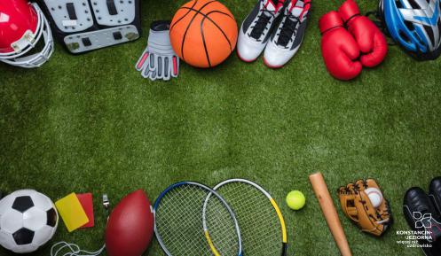 na trawniku rozłożone różnorodne sprzęty sportowe takie jak piłki, rękawice, buty sportowe, kask i ochraniacze