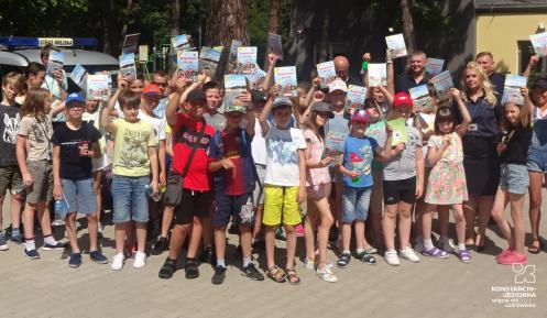 Grupa dzieci z książkami w rękach, na tle drzew i budynku szkoły