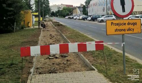 Remont chodnika. Na pierwszej części chodnika położona jest kostka brukowa, dalej widać ziemie, na której dopiero będzie ona kładziona. Wejście na chodnik jest ogrodzone, biało czerwonym szlabanem.