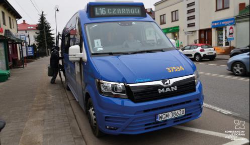 Niebieski bus stoi na przystanku, ma otwarte boczne drzwi, nad przednią szybą wyświetlacz z numerem linii L16 i nazwami przystanków – początkowego i końcowego – Czarnów.