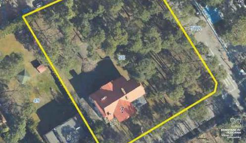 Zdjęcie terenu robione z góry z dużej odległości. Żółtą linią w kształcie prostokąta wyznaczony jest teren działki. Na działce rośną wysokie drzewa oraz stoi dom z pomarańczowym dachem.