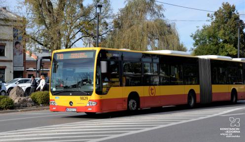 Ulica, po której jedzie czerwono-pomarańczowy autobus komunikacji miejskiej. Nad jego przednią szybą wyświetla się napis: 710 Piaseczno Targowisko.