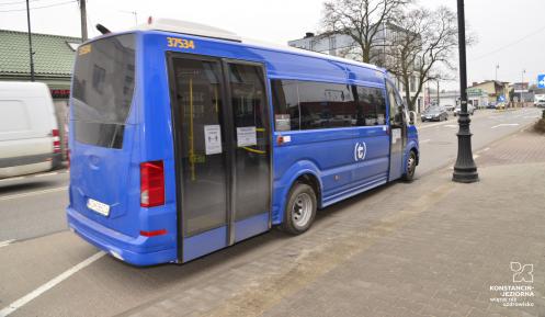 Niebieski autobus niskopodłogowy odjeżdża z przystanku, w tle budynki i ulica.