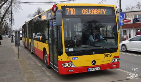 Ulica, po której jedzie czerwono-pomarańczowy autobus komunikacji miejskiej. Nad jego przednią szybą wyświetla się napis: 710 Osiedle Kabaty.