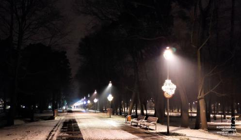 Aleja spacerowa nocą. Po prawej stronie widoczne są latarnie, na których zamontowano zwisające ozdoby świąteczne. 
