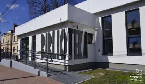 Przestrzeń miejska. Budynek biblioteki z białą elewacją i dużymi oknami.