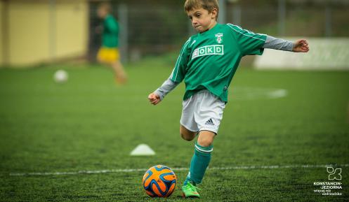 Dziecko ubrane w strój sportowy kopie piłkę na boisku. 