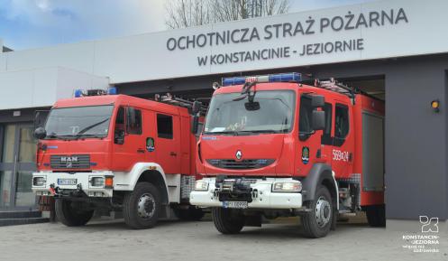 Dwa wozy strażackie, stojące przed dużym odnowionym budynkiem Ochotniczej Straży Pożarnej w Konstancinie-Jeziornie. 