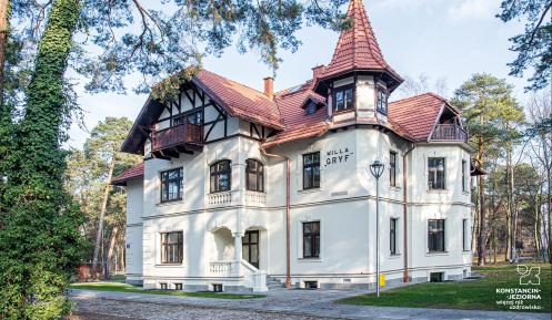 Budynek z czerwoną dachówką i wieżyczką, w otoczeniu drzew.