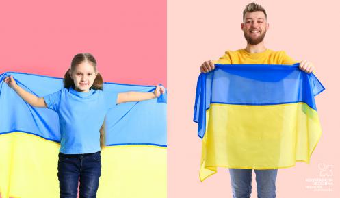 Dziewczynka i mężczyzna trzymają w rękach ukraińską flagę (płótno z dwoma poziomymi pasami: niebieskim i żółtym)