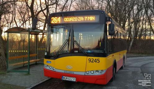 Pomarańczowo-czerwony autobus stoi na przystanku, nad przednią szybą wyświetlany jest numer linii 264 i informacja: odjazd za 7 minut..