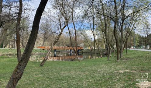 Widok Parku Zdrojowego, trawnik, drzewa, w tle rzeka i most
