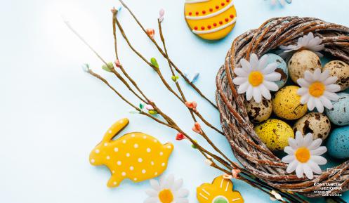 Grafika wektorowa: koszyczek wiklinowy z kolorowymi jajkami. Obok leżą bazie oraz zajączek z ciasta.
