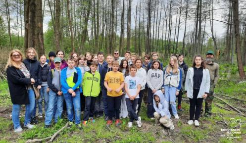 Grupa młodzieży stojąca w grupie razem z dwójką nauczycieli, pozujący do zdjęcia na tle podmokłego lasu.