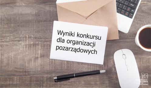 Na biurku stoi komputer, myszka i kubek z kawą na klawiaturze leży otwarta koperta i list